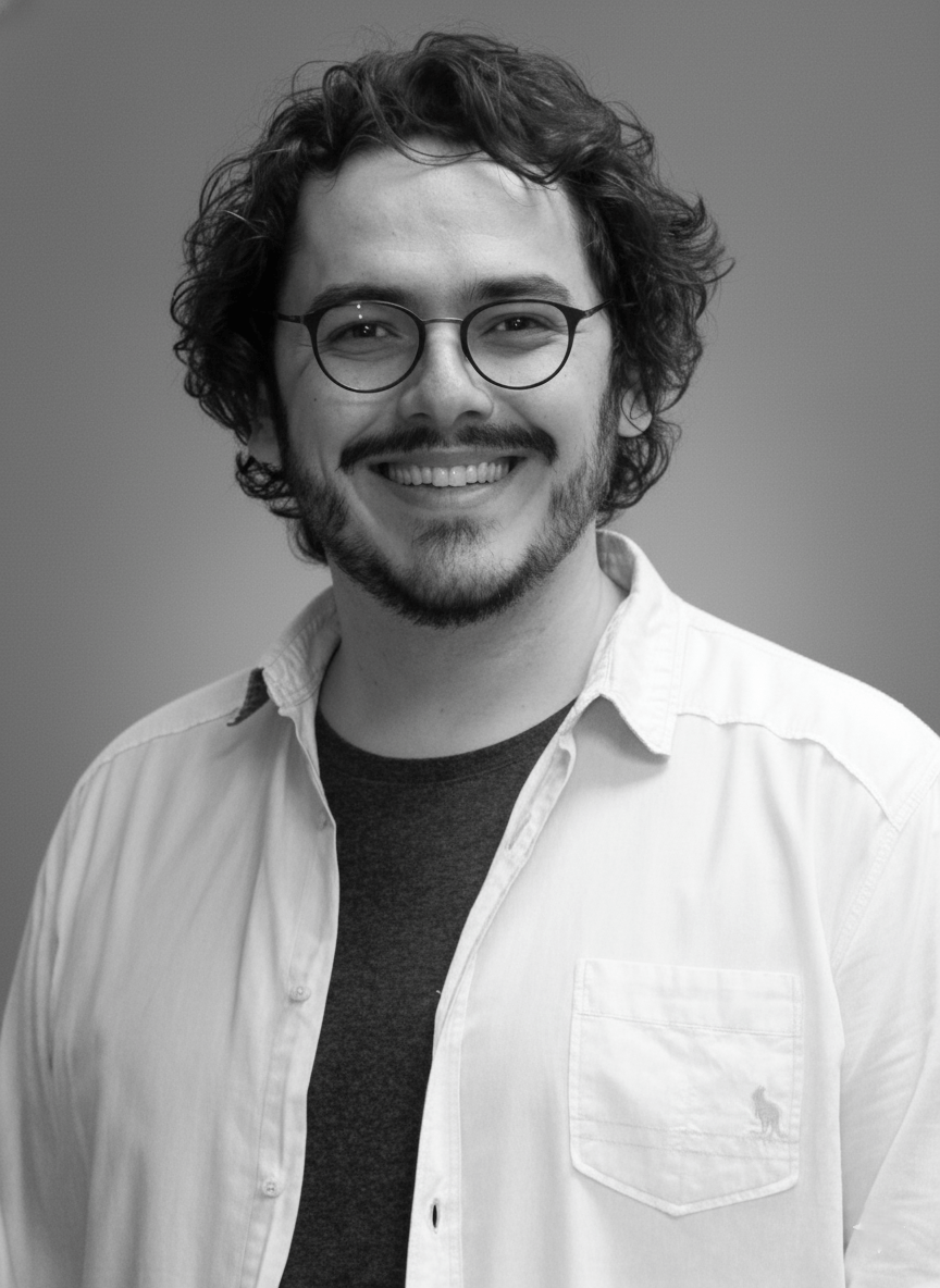 Homem branco, com cabelo preto e barba. Usa óculos e está sorrindo.