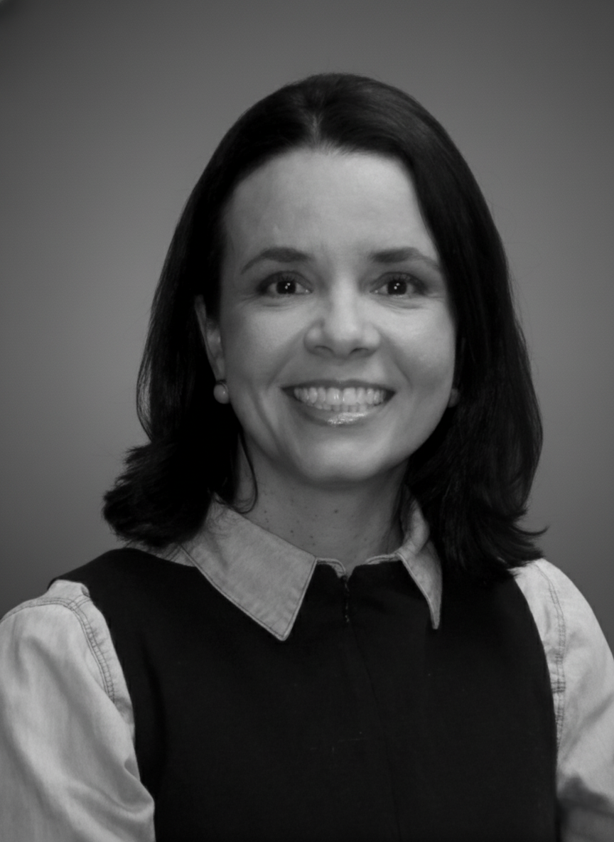 Mulher branca, com cabelo preto na altura dos ombros. Está sorrindo.