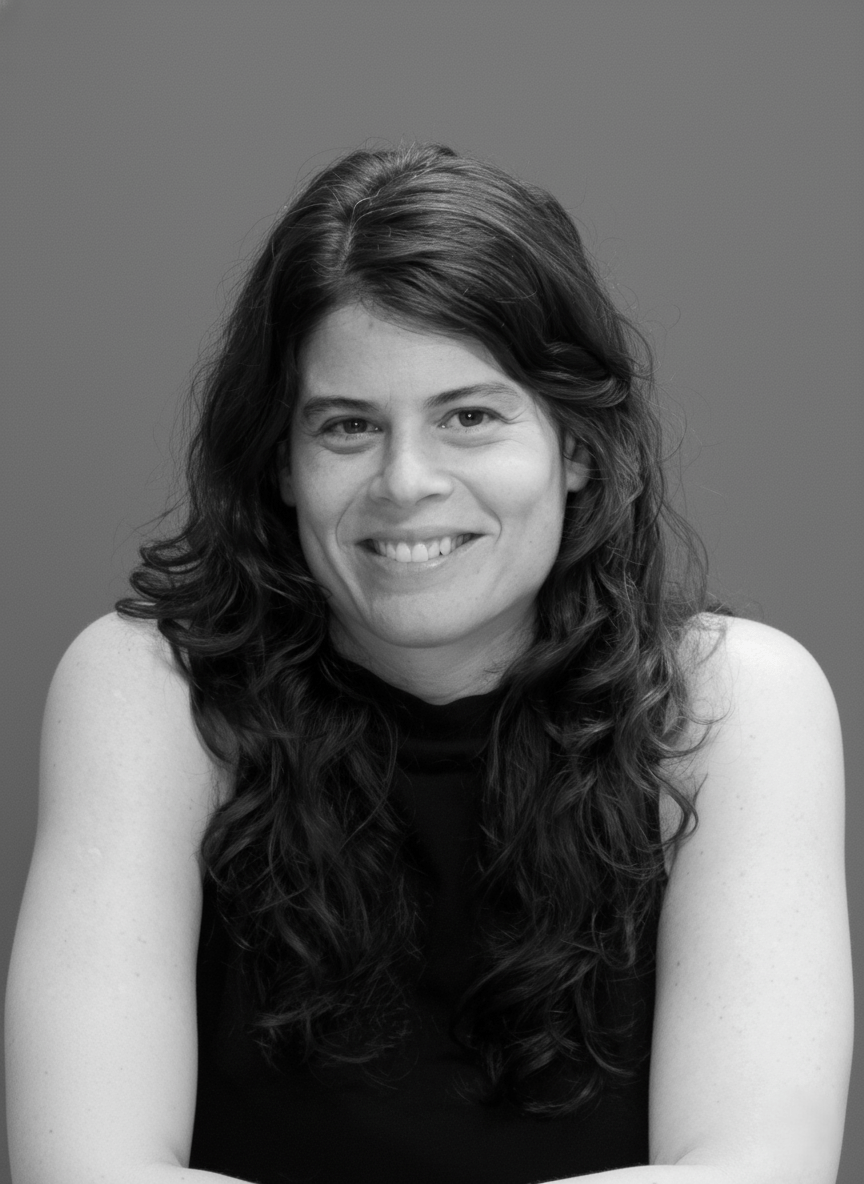 Mulher branca, com cabelos longos ondulados. Está sorrindo.